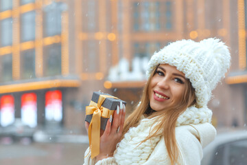 Cheerful lady holding a gift box during the snowfall