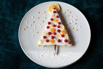 Zitronenkuchen dekoriert als Christbaum mit Johannisbeeren, Zitrone, Kumquat, Zuckerguss und Sternen aus Zucker auf einem weißen Teller