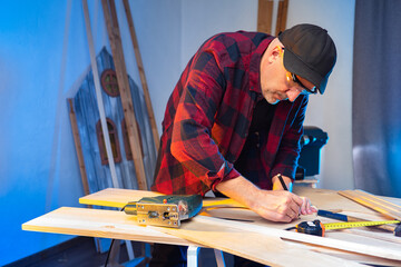 A carpenter works in a workshop. A man marks up the boards. Marking of wooden bars. Production of...