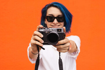 Close up portrait of a smiling pretty girl taking photo on a digital camera isolated over orange...