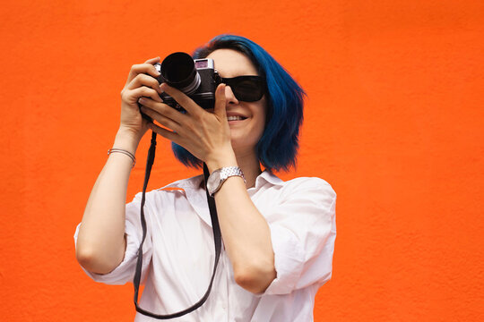 Close up portrait of a smiling pretty girl taking photo on a digital camera isolated over orange background
