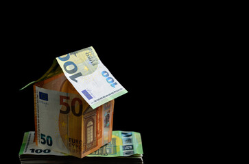 Abstract architecture - house with Euro banknotes on the black background. Simple, isolated object with copy space perfect for illustrating various concepts and ideas. Selective focus (shallow DOF).