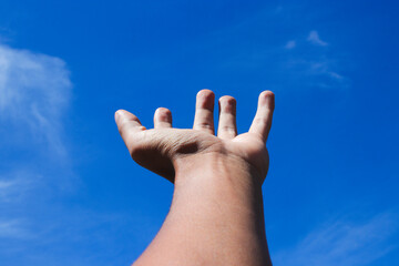 An Asian Man Hand Gesture Trying to Reach the Sky with Clear Blue Sky on a Sunny Day to Illustrate Dream Catcher, Success, and Struggle