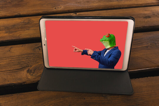 tablet on a wooden table in a garden showing a man with a frog mask on a red background