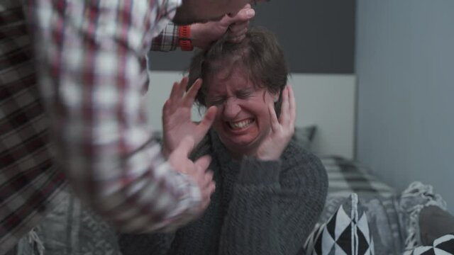 Abusive man holding hair of scared wife beaten on his face, screams and threatens with his hand. Female with bruises on her face victim suffers from a violent male who roughly grabs her by the hair.