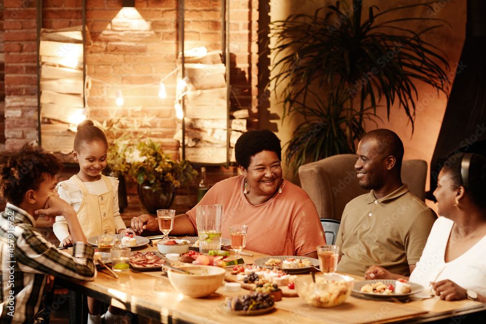 Wall mural warm toned portrait of big african-american family sitting at table outdoors and enjoying dinner tog