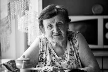 Portrait of an old woman sits at a table in her home. Black and white photo.