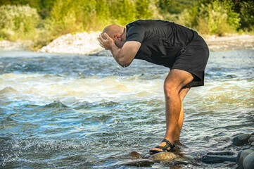 Male traveler washes his face with mountain stream water. Man tourist sitting on rocks near mountain river and refreshing himself. High quality photo