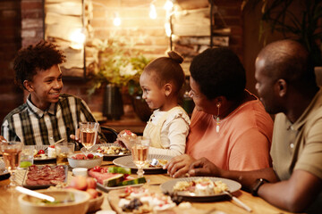 Warm toned portrait of happy African-American family enjoying dinner together outdoors with focus...