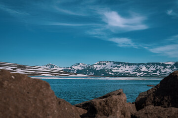 Fototapeta na wymiar Panoramic frog view of Heidharvatn lake in eastern iceland, glacial lake with some blocks of ice floating and majestic mountains and road next to it.