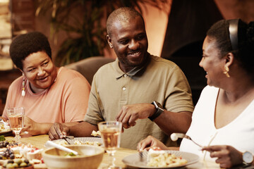 Warm toned portrait of happy African-American family enjoying dinner together outdoors at evening