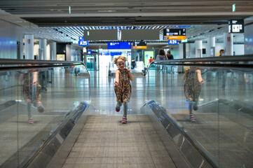 Cute blonde girl running on speed escalator at airport.