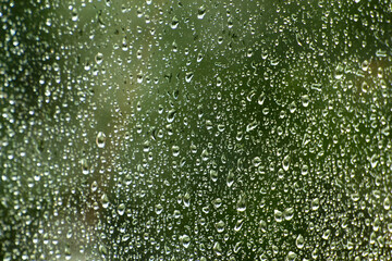 Raindrops run down the glass. Green blurred background