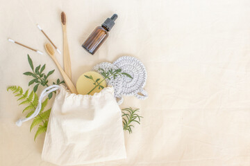 Biodegradable beauty and hygiene items coming out of a natural raw cotton bag: bamboo toothbrush, dye-free bar soap, cotton swabs, eco pads for skin care and natural green leaves