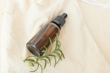 amber glass of rosemary essential oil on a natural unbleached cotton fabric
