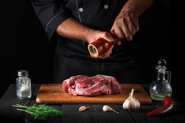 Professional chef cooking raw meat fillet and adding pepper or chili for marinade on black...