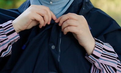 The woman is buttoning a black raincoat. Close-up.