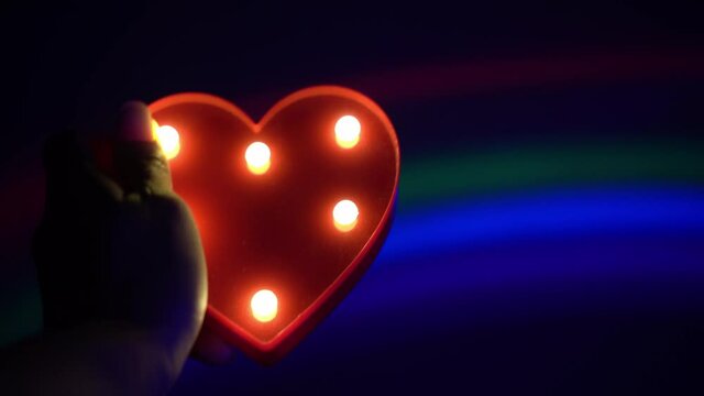 A man left hand hold love shape led in background rainbow light