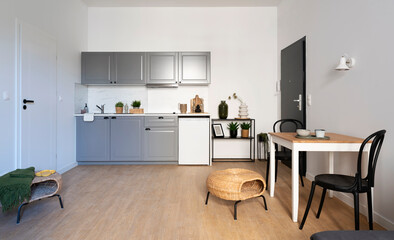 Modern kitchen interior with dinig room in small apartment with wooden floor and white wall. Stylish furniture in kitchen with table and chairs.