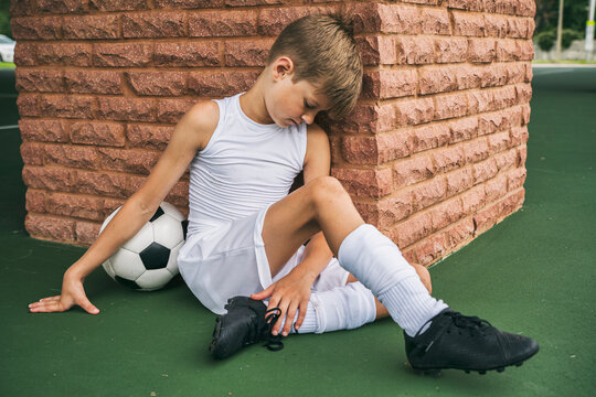 Exhausted young soccer boy leans against wall to rest after playing game 