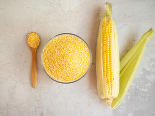 corn grits in a bowl and in a wooden spoon with an ear of corn