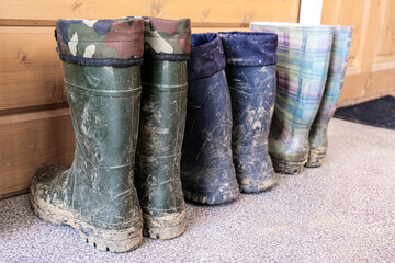 A row of muddy dirty rubber boots at a country house