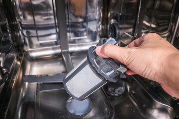 A hand taking out dishwasher filter to clean it, dis washer cleaning concept, kitchen home appliances care and maintenance