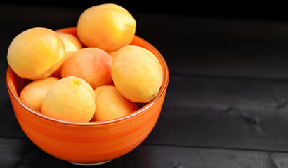 Ripe apricots in a bowl on a wooden background