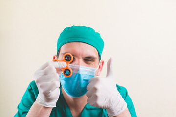 Doctor in green surgeon suit and protective breathing mask with spinning orange spinner toy in his...