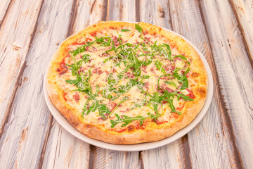 Iberian ham pizza with arugula, mozzarella cheese and grated cheese with tomato on wooden table