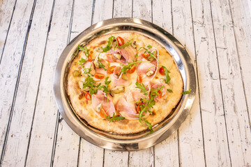 Italian pizza with pork, artichoke hearts, cherry tomatoes, arugula leaves and mozzarella cheese with olive oil