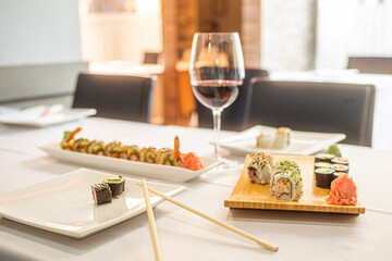 sushi uramaki roll with ginseng and wasabi, chopsticks and glass of wine in a restaurant with white tablecloth