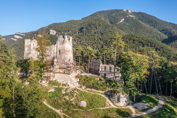 Aerial view of medieval Blatnica Gothic hilltop castle ruin above the village in a lush green forest area with towers and restoration work in Slovakia