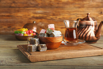 Bowl with tasty Turkish delight and glass of tea on wooden background