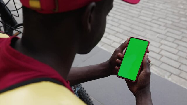 Back view of young african american delivery man using mobile phone with vertical green mock up screen chroma key - Small business and delivery service concept. High quality 4k footage