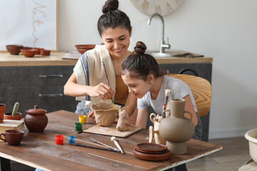 Little girl with her mother painting ceramic pot at home