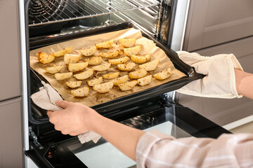 Woman taking baking tray with fresh potato out of oven