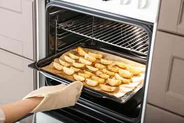 Woman taking baking tray with fresh potato out of oven