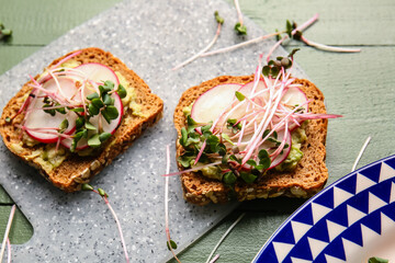 Tasty sandwiches with radish and micro green on color wooden background