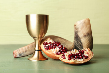 Shofar with sacramental goblet for wine and pomegranate on color wooden background. Rosh hashanah...