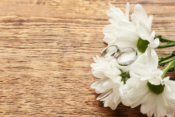 Wedding rings and beautiful flowers on wooden background