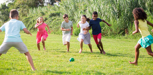 Boys and girls playing football on green grass together outdoors.