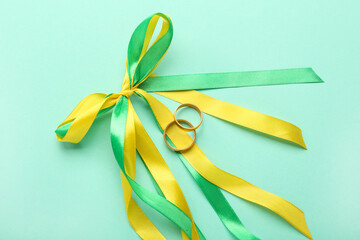 Wedding rings and bow made of ribbons on color background