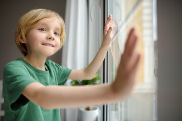 Portrait of little boy standing in front of window at home. Cute child is smiling.