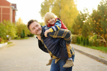 Fototapeta premium Little boy and his father having fun during stroll on sunny autumn day. The father rides the child on own back. Hiking with kids.