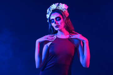 Young woman with painted skull on her face against dark background. Celebration of Mexico's Day of the Dead (El Dia de Muertos)