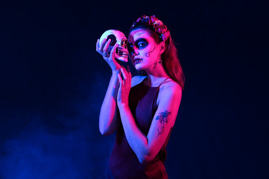 Young woman with painted face and sugar skull for Mexico's Day of the Dead (El Dia de Muertos) on dark background