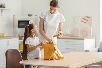 Mother packing school lunch for her little daughter at home