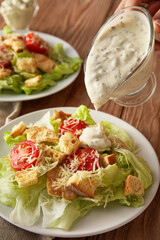 Adding sauce onto plate with tasty Caesar salad on wooden background