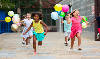 Fototapeta premium Group of happy kids running through streets with balloons in hands.